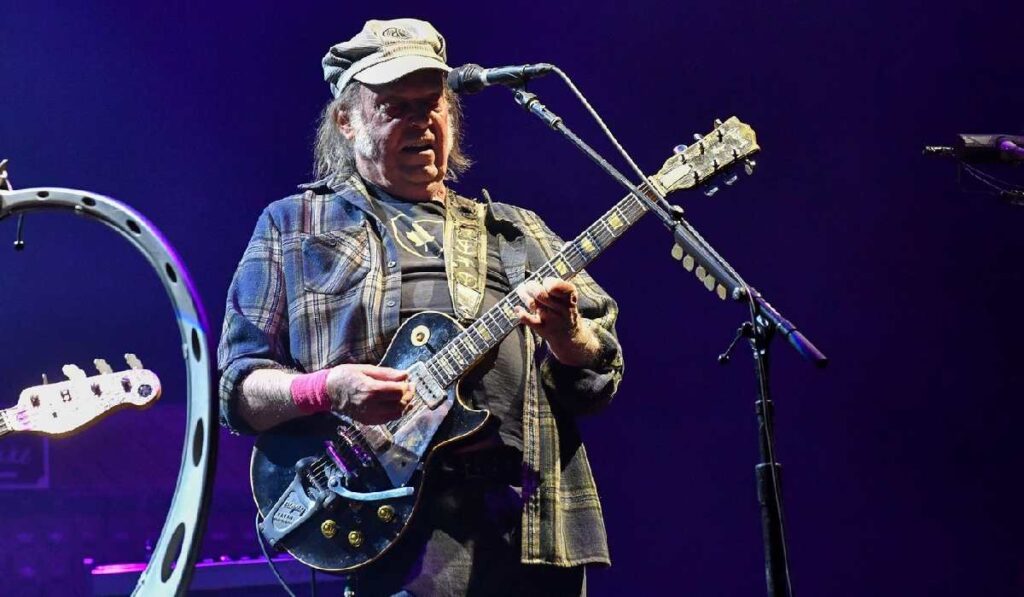 Cântărețul Neil Young ține o chitară în mână și cântă la un microfon la un festival
