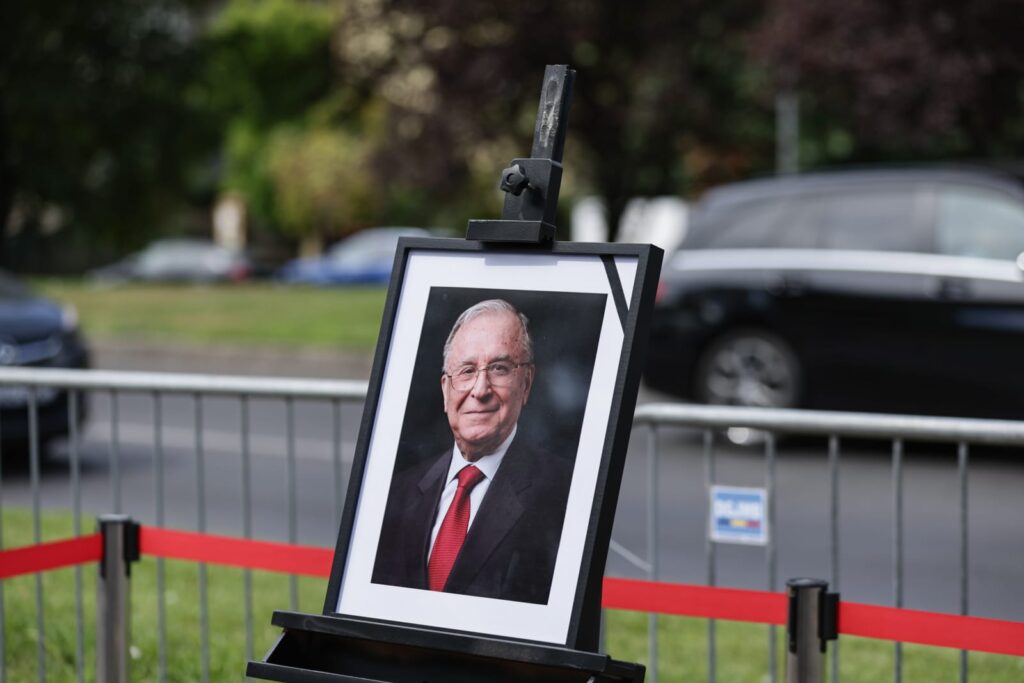 imaginea lui ion iliescu, într-o ramă neagră cu o banderolă neagră pe colt. rama cu imaginea este asezata într-un chenar realizat dintr-o paglică roșie, în parcarea Palatului Cotroceni, 6 august 2025