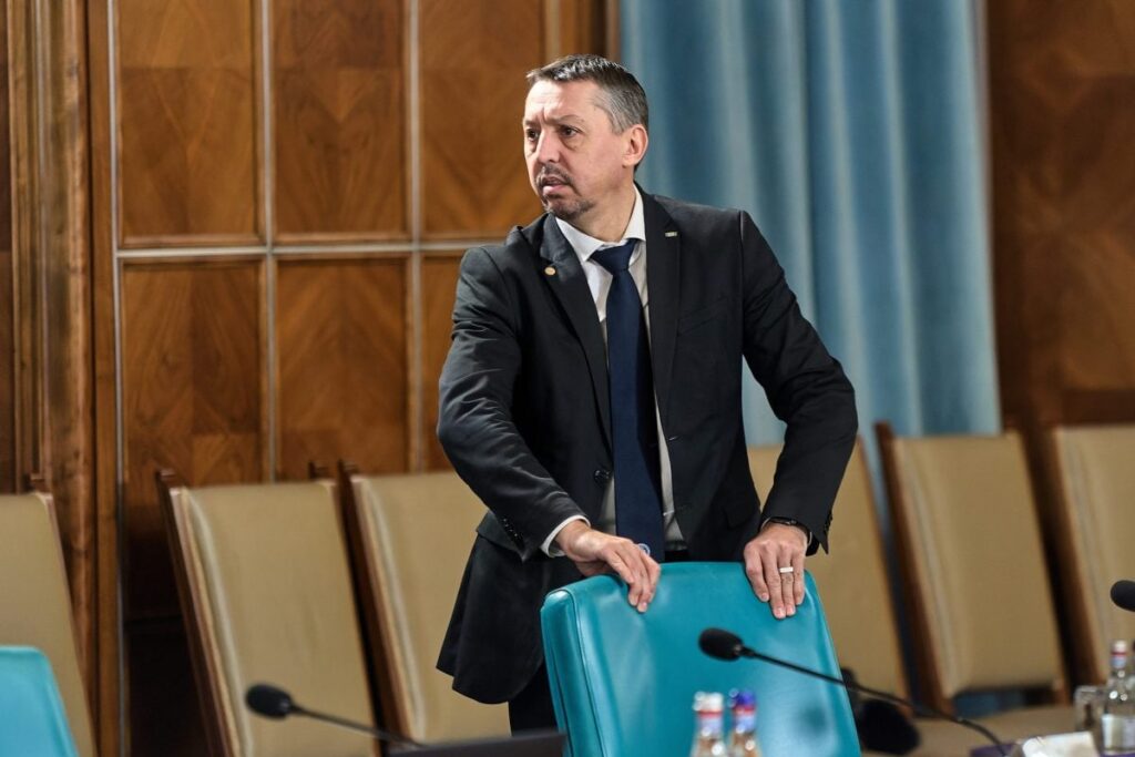 Ministrul Educației, Daniel David, stă în picioare, în spatele unui scaun gol, intr-o sală de conferințe