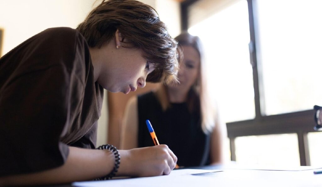 Elev care se concentrează asupra testului, scriind pe hârtie, cu ajutorul profesorului