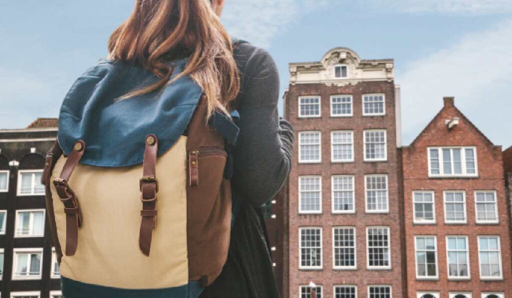 O tânără cu un rucsac se uită la casele tradiționale din Amsterdam, capitala oficială a Țărilor de Jos