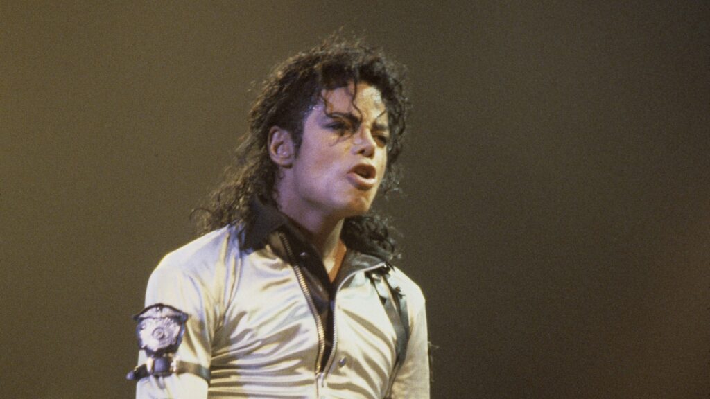 Michael Jackson în timpul unui concert, îmbrăcat într-o bluză aurie, cu guler maro și detalii de piele pe braț