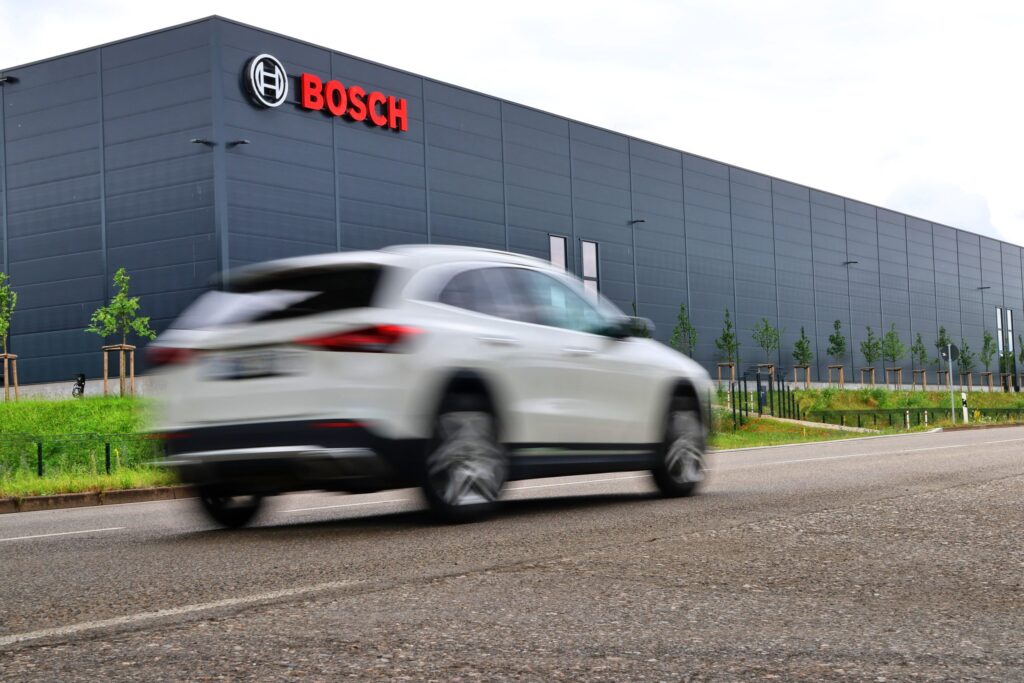 Fabrică Bosch cu logo-ul companiei prin fața căruia trece un Audi alb
