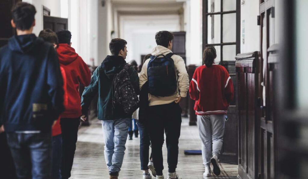 Elevi care se plimbă pe holuri, într-un liceu din București. Ei poartă ținută casual și au rucsac