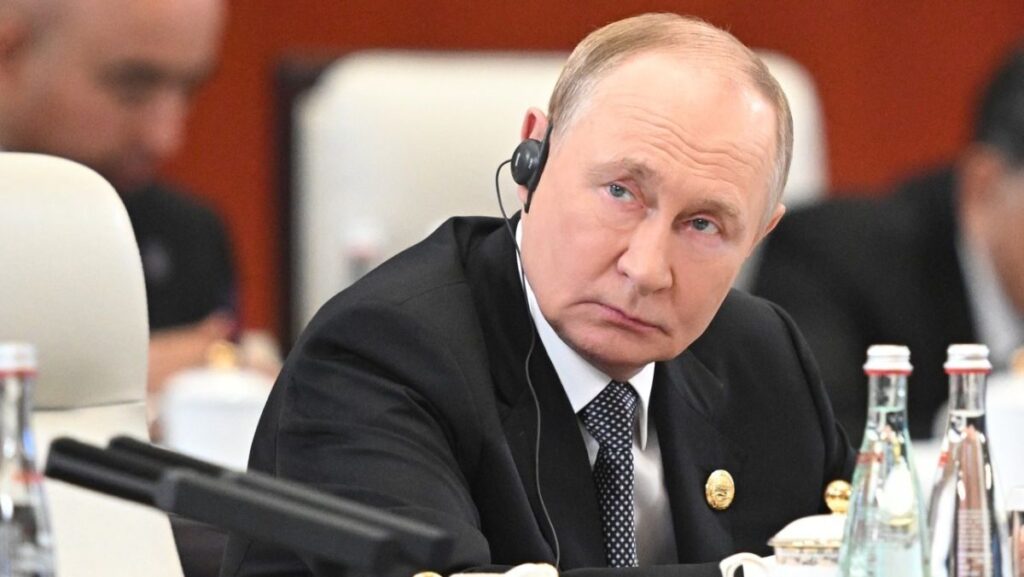 președintele Rusiei, Vladimir Putin, în sacou negru si cravata, cu o casca pe ureche si insigra in piept, asezat la masă la summitul Organizației de Cooperare de la Shanghai (SCO) de la Tianjin, pe 1 septembrie 2025