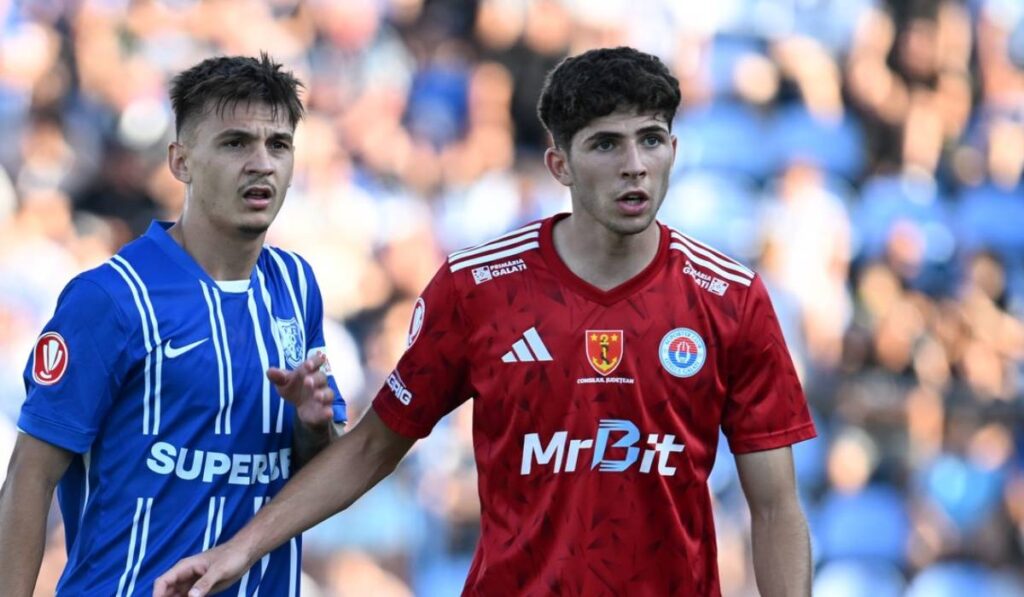 În imagine este fotbalistul Ștefan Bană, pe teren, purtând tricoul vișiniu specific Oțelul Galați, alături de un alt fotbalist de la Farul Constanță.