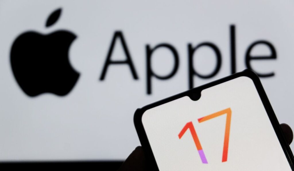 Un logo colorat al cifrei 17, pe display-ul unui telefon, in fata unui fundal pe care e afșiat logo-ul Apple.