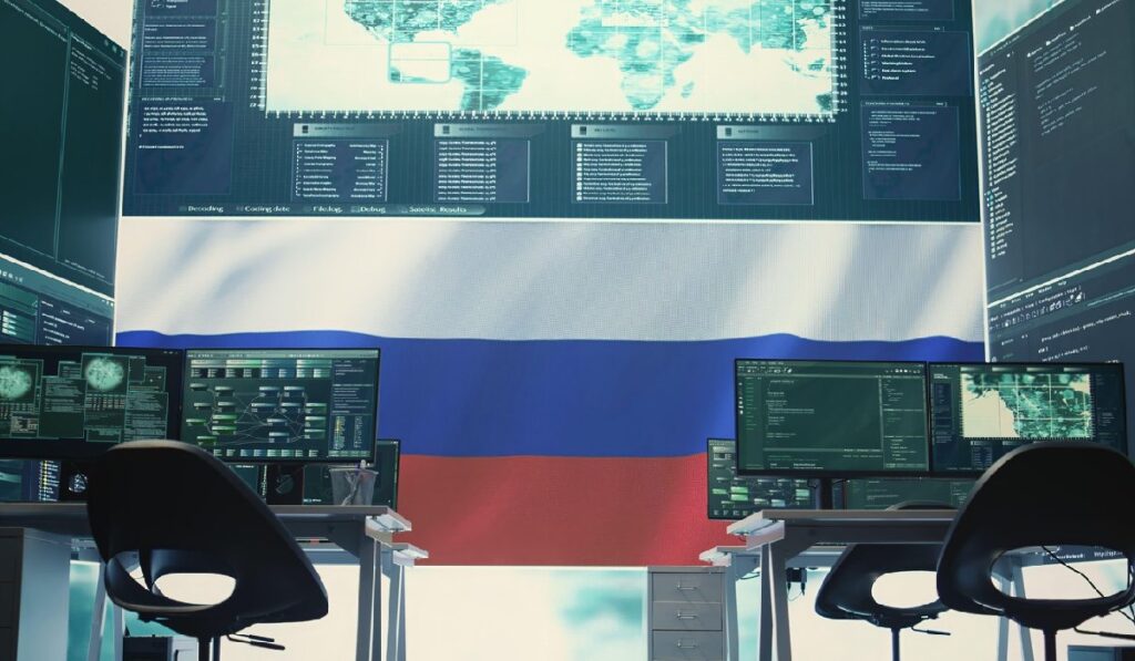 Cameră goală, folosită pentru hacking, cu steagul Rusiei pe ecranul mare, evidențiind terorismul cibernetic și dezinformarea.