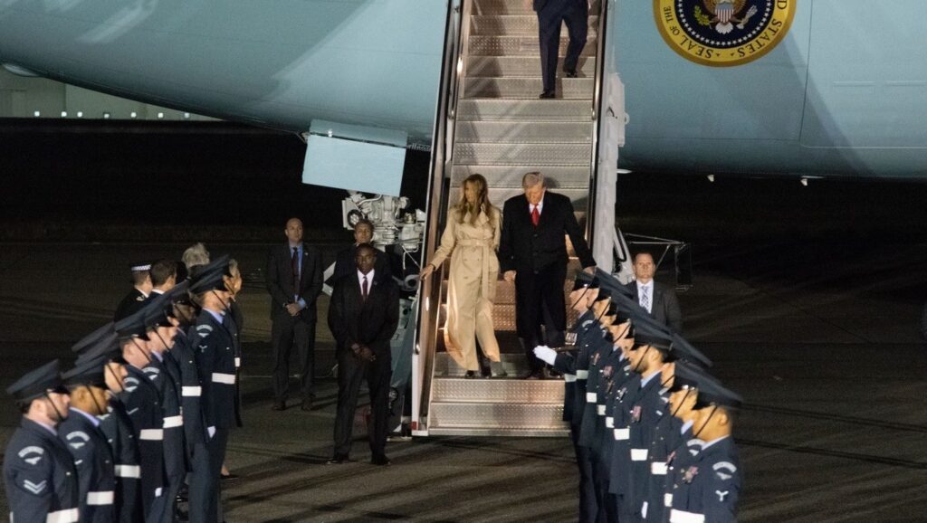 Președintele Donald Trump coboară din Air Force One după aterizarea pentru a doua sa vizită de stat în Marea Britanie. Alaturi de el este sotia Melania Trump. In stanga si in dreapta scarii avionului mai multi soldati fac de garda