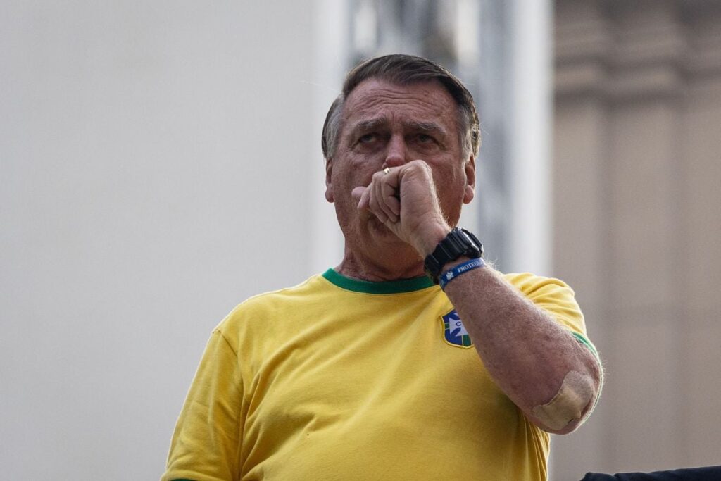 Îmbrăcat cu un tricou galben al naționalei de fotbal a Braziliei, Jair Bolsonaro duce la gură mâna stângă cu pumnul strâns, septembrie 2024