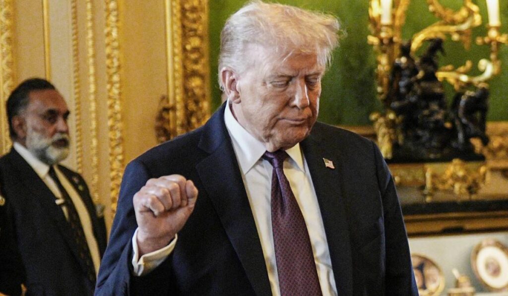 În imagine se vede cum președintele american Donald Trump este supărat. Trump este ămbrăcat într-un costum negru i o cămașă vișinie și merge pe unul din holurile palatului Winsdor