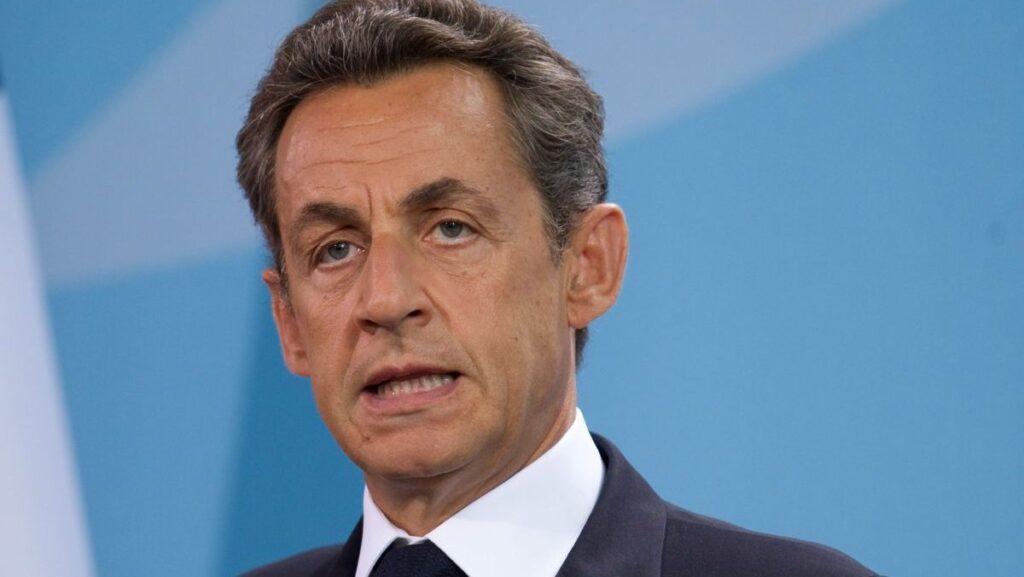Nicolas Sarkozy, la acea vreme președintele Franței, îmbrăcat la costum, vorbește la o conferință de presă la Cancelaria din Berlin, având în spate un fundal bleu, 17 iunie 2011