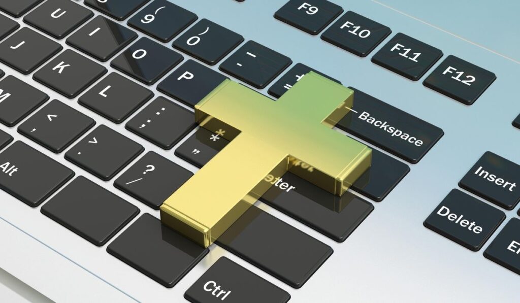 Creștinism și tehnologie. Cruce de aur pe tastatura laptopului.