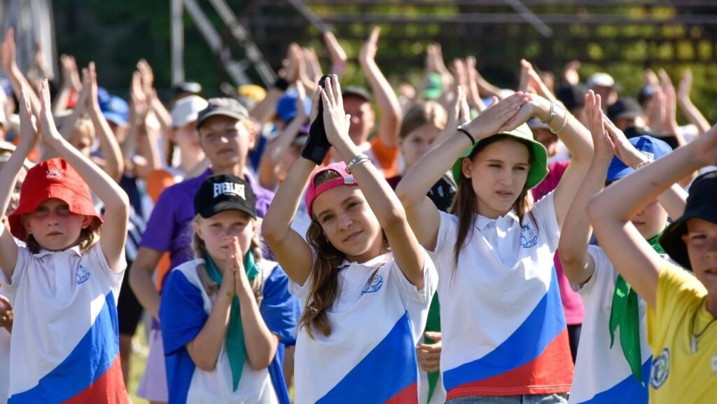 Imagine cu mai mulți copii care au mâinile ridicate și sunt îmbrăcați cu tricouri care au drapelul Rusiei