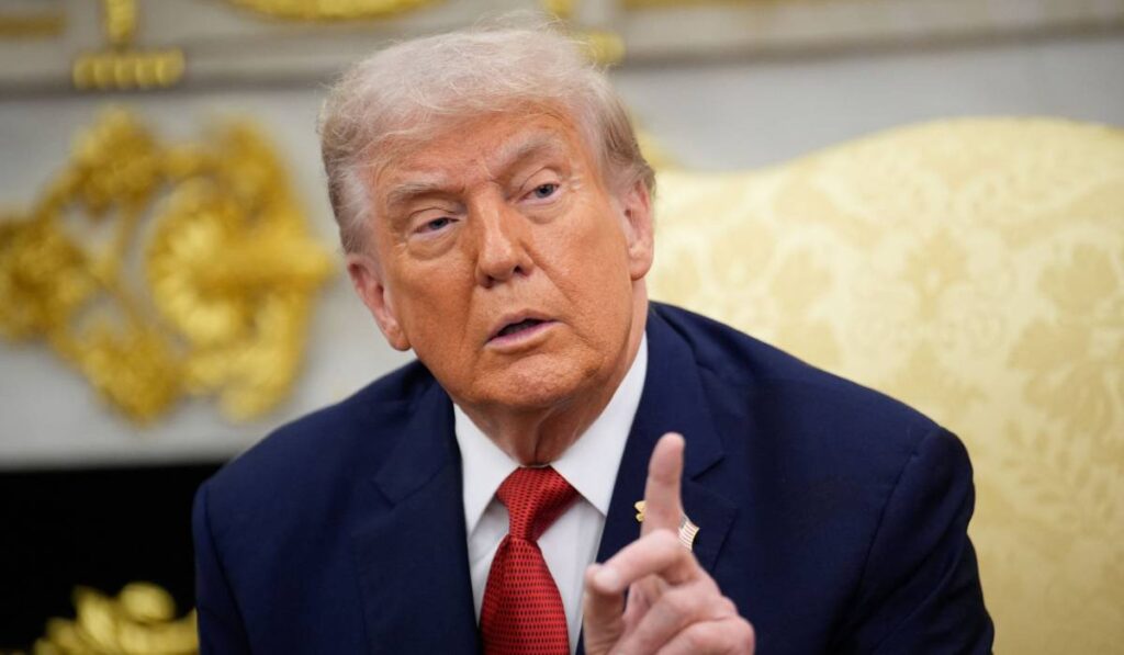 Președintele american Donald Trump stând pe canapeaua galbenă din Biroul Oval, ține degetul arătător ridicat și explică ceva