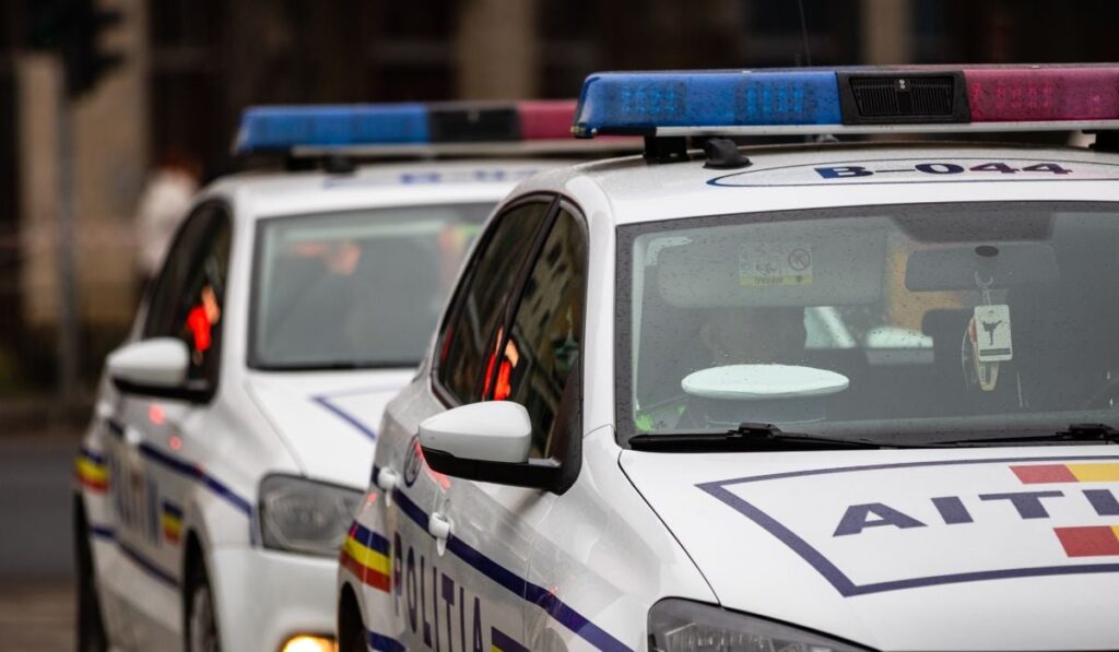Două mașini de Poliție, una în fața celeilalte, în prim plan, pe o stradă