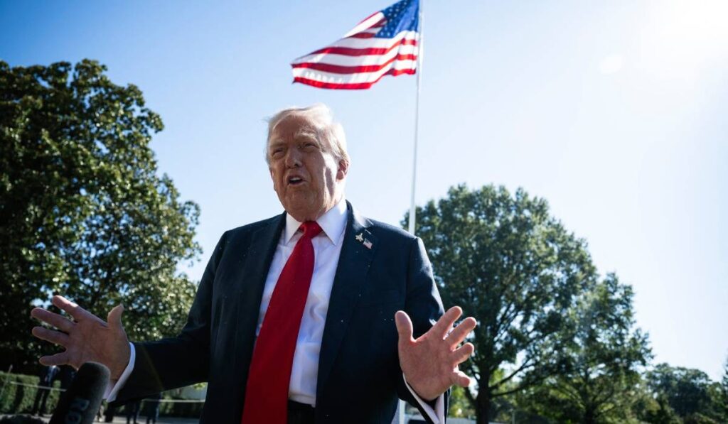 Președintele american Donald Trump în curtea de la Casa Albă, este fotografiat de jos, iar în spatele său se vede steagul Americii