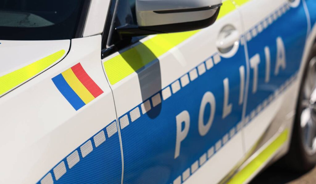 Ușa unei mașini de poliție parcate, cu însemnele Poliției Române și steagul României