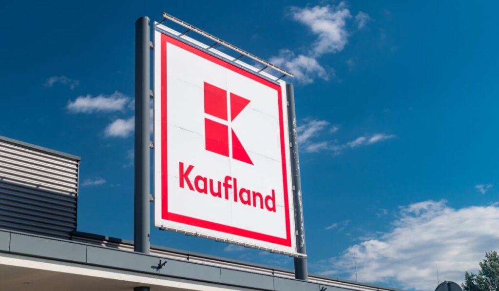 Care este produsul de la Kaufland la prețul de doar 69,99 lei care îți încălzește casa Sigla Kaufland este vizibilă pe fundalul unui cer albastru senin. Panoul este montat pe o structură metalică deasupra unei clădiri.