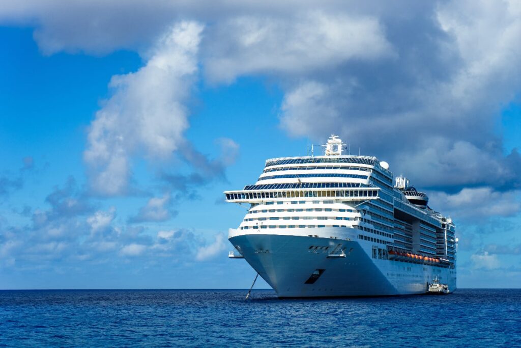 Cum a ajuns o pensionară să moară singură pe o insulă pustie O navă de croazieră mare, albă și modernă, plutește pe suprafața unei mări de un albastru intens sub un cer parțial noros. Silueta impunătoare a vasului domină peisajul marin, sugerând un moment de odihnă sau ancorare în larg.