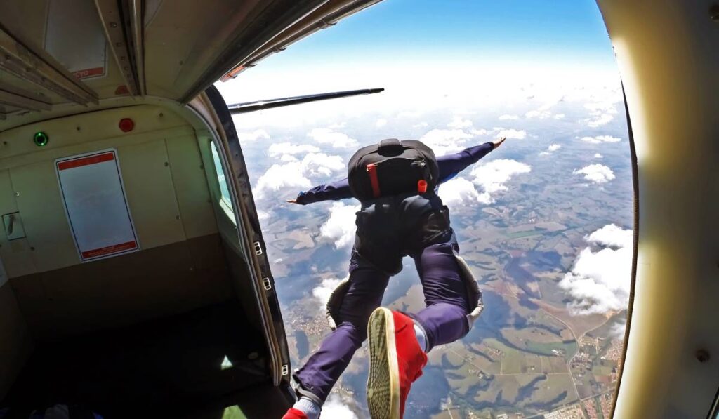 Un bărbat care sare din avion, are parașuta în spate și o pereche de pantaloni albaștrii