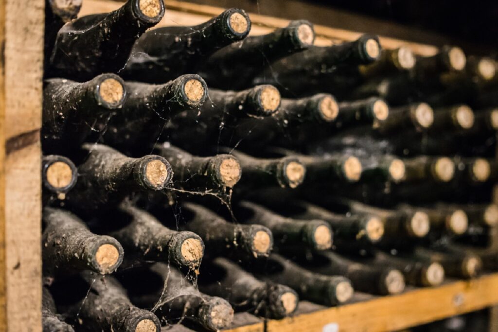 Cum se învecheşte vinul Cum se învecheşte vinul - Imagine cu sticle de vin acoperite de praf, aşezate orizontal pe un raft, pentru învechire