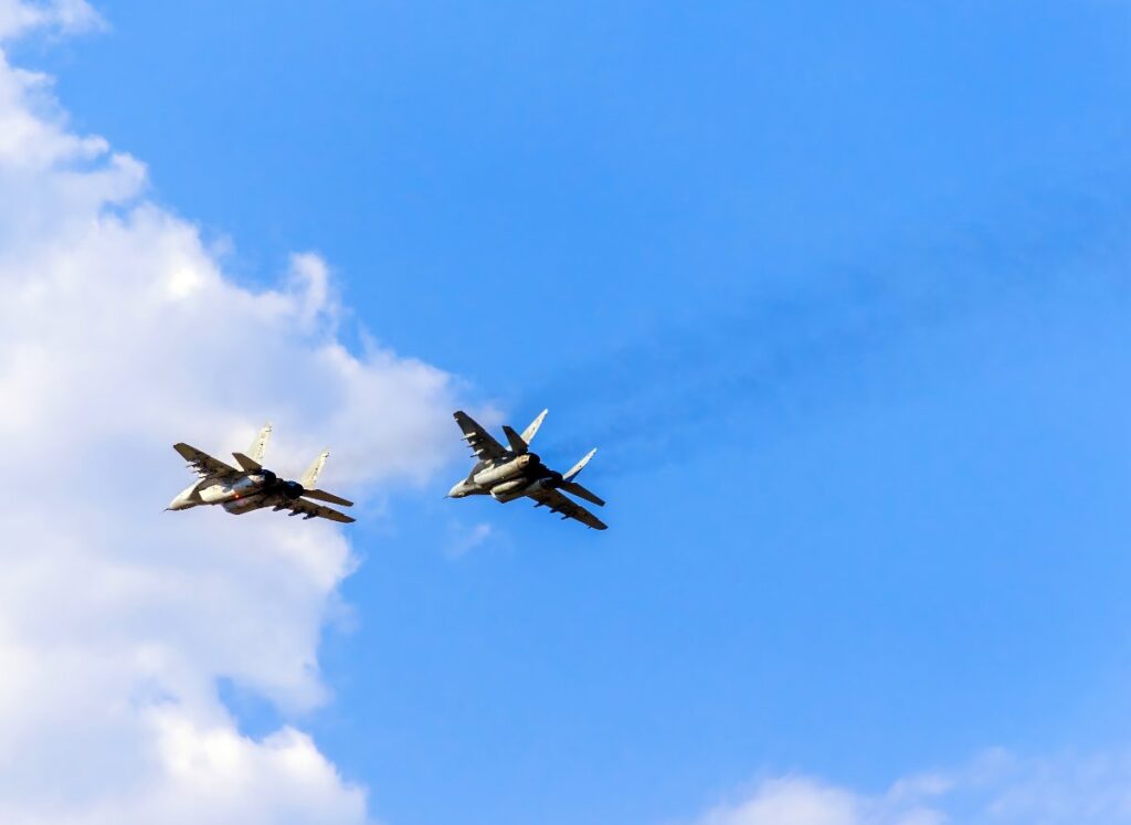 Două avioane ale Marinei SUA se prăbușesc la doar 30 de minute unul de celălalt Două avioane de vânătoare zboară în formație strânsă pe un cer predominant albastru, parțial acoperit de câțiva nori albi. Avioanele, văzute de jos, lasă în urmă urme discrete de fum și se deplasează la o viteză mare, probabil executând un zbor demonstrativ sau o misiune.