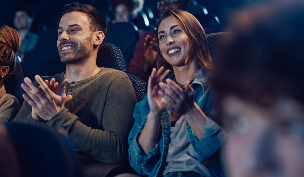 Oameni într-o sală de teatru care zâmbesc și aplaudă