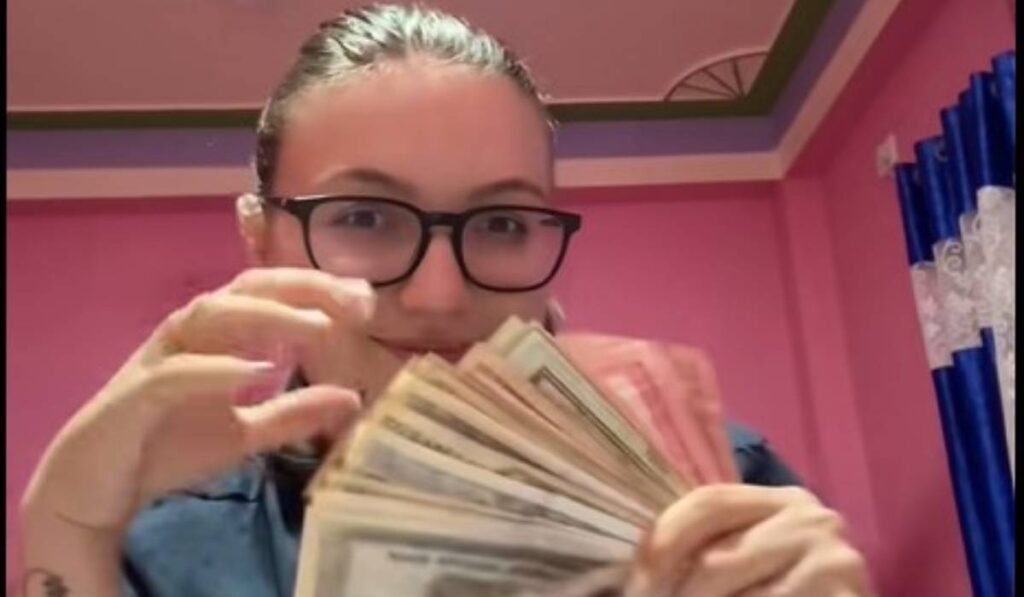 Românca măritată cu un nepalez în timp ce arată la cameră un teanc de bani nepalezi, poartă ochelari și un tricou albastru