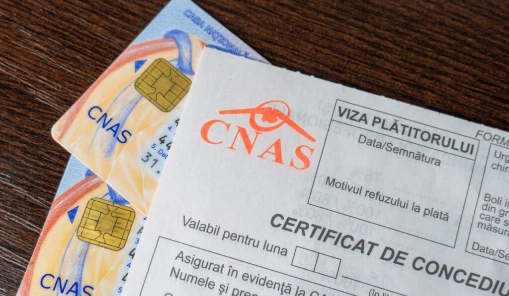 Două carduri pentru asigurarea de sănătate din România, așezate pe un birou, lângă un formular