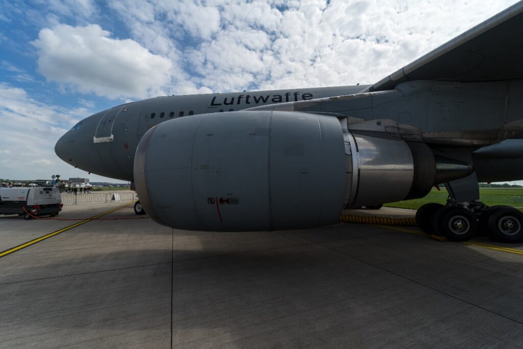 Transportul unui Airbus uriaș, scos din uz, blochează traficul în nordul Germaniei pentru 3 nopți: va fi transformat în restaurant Imaginea prezintă o secțiune a unui avion militar de mari dimensiuni, fotografiat de la nivelul solului, evidențiind motorul masiv și trenul de aterizare. Pe fuselajul gri al aeronavei se poate citi clar inscripția "Luftwaffe", indicând apartenența sa la forțele aeriene germane, în timp ce pe fundal se observă o vreme parțial noroasă și câteva vehicule de suport la sol.