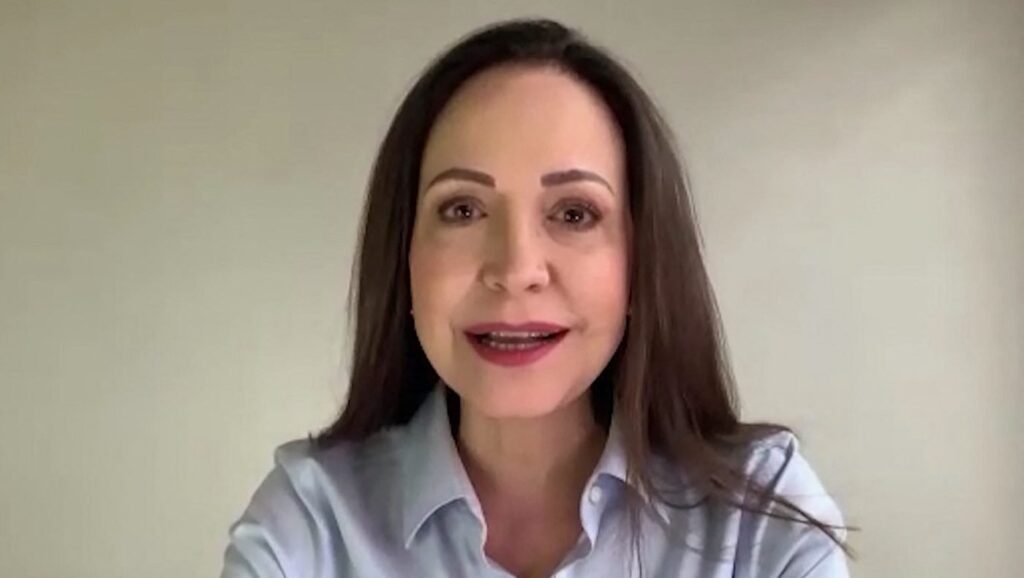 Maria Corina Machado in camasa albastra, cu parul lung, zambeste larg la camera