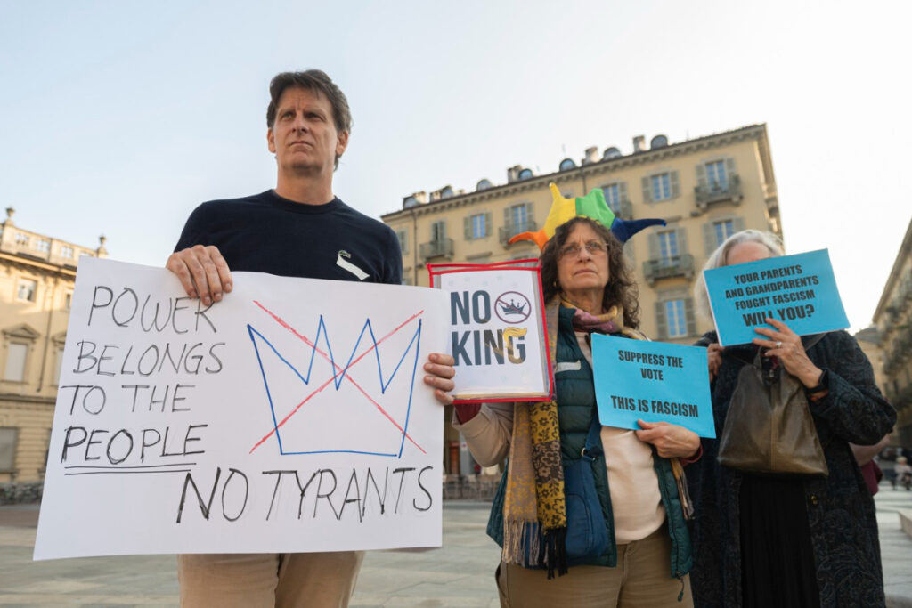 Imaginea surprinde trei protestatari, probabil în Europa, care țin pancarte cu mesaje politice în limba engleză. Mesajul principal mare este „POWER BELONGS TO THE PEOPLE NO TYRANTS” (Puterea aparține poporului, nu tiranilor), în timp ce celelalte pancarte fac referire la fascism și la istoria luptei pentru democrație.