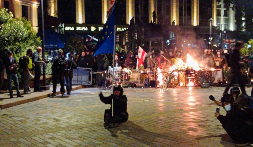 Protestatarii din Tbilisi izolați de polițiști, au dat foc unor piese de mobilier stradal, o persoană stă jos în mijlocul străzii cu un steag în mână