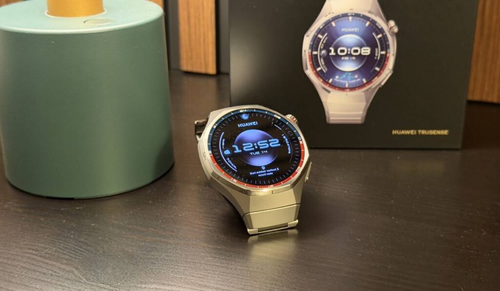 Un smartwatch Huawei GT 6 Pro cu curea de metal, pe un fundal de lemn, cu cutia sa de culoare neagră în spate.
