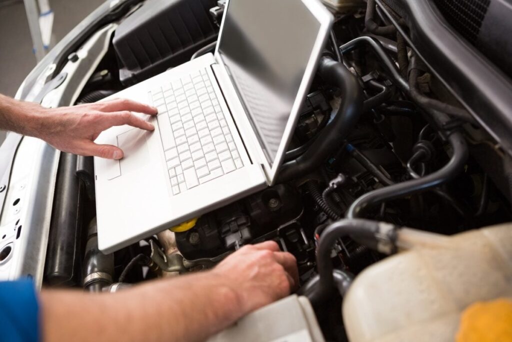 Mecanic auto care calibrează motorul unei mașini cu ajutorul unui laptop