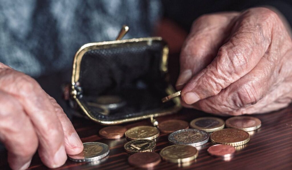 O femeie cu venituri extrem de mici, în timp ce își numără monedele de câte un euro dintr-un portofel. Banii primiți din ajutorul social sunt întinși pe o masă maro