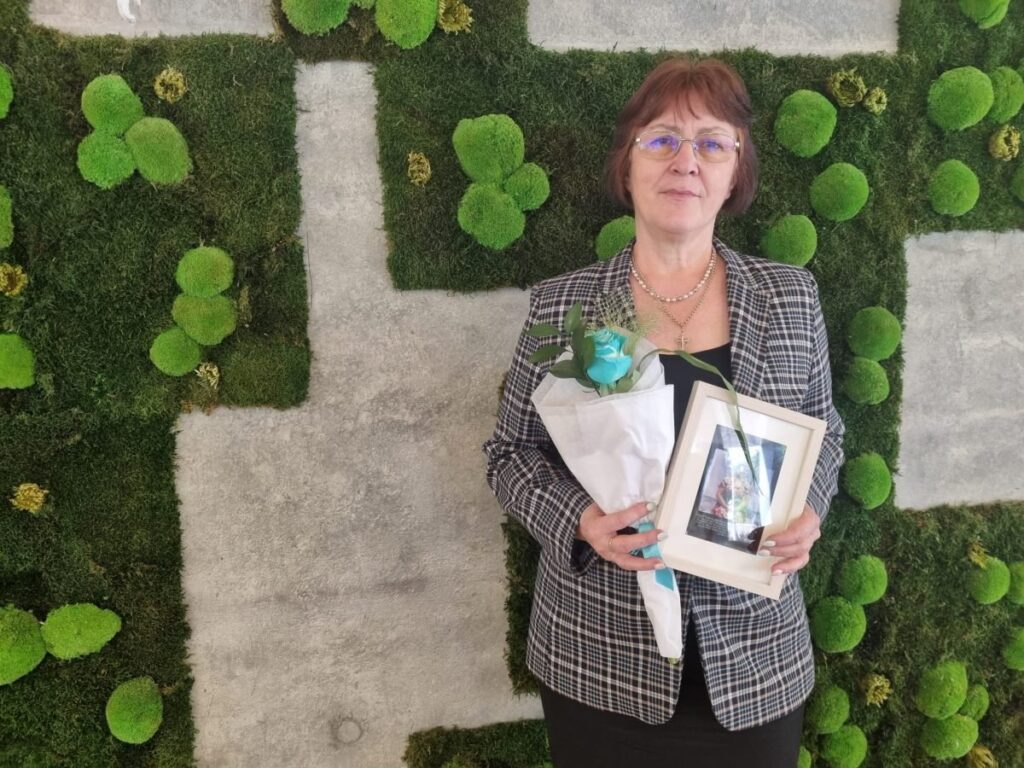 Femeie care ține în brațe un tablou ți un buchet de flori