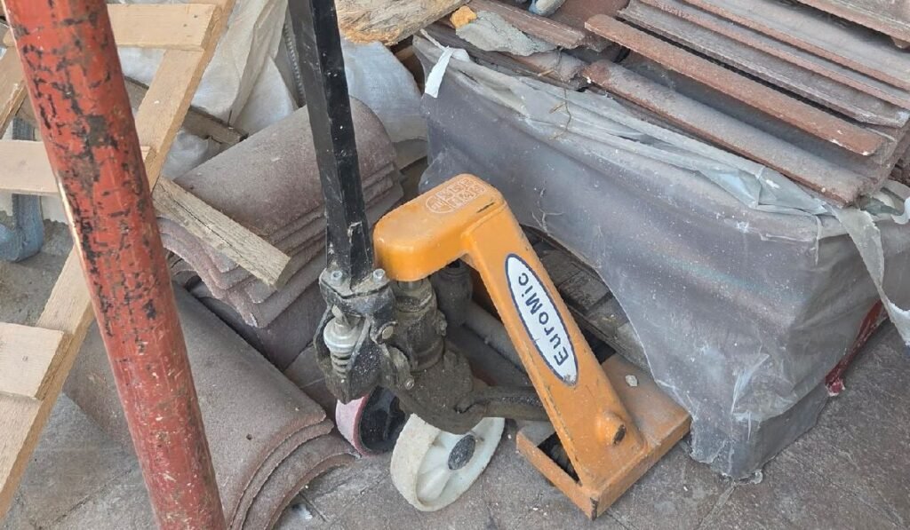 Incredibil ce postează pagina asta! Fotografie cu un șantier aglomerat, cu o țeavă metalică neagră, o clemă galbenă „Clawhamer” și diverse materiale de construcție împrăștiate.