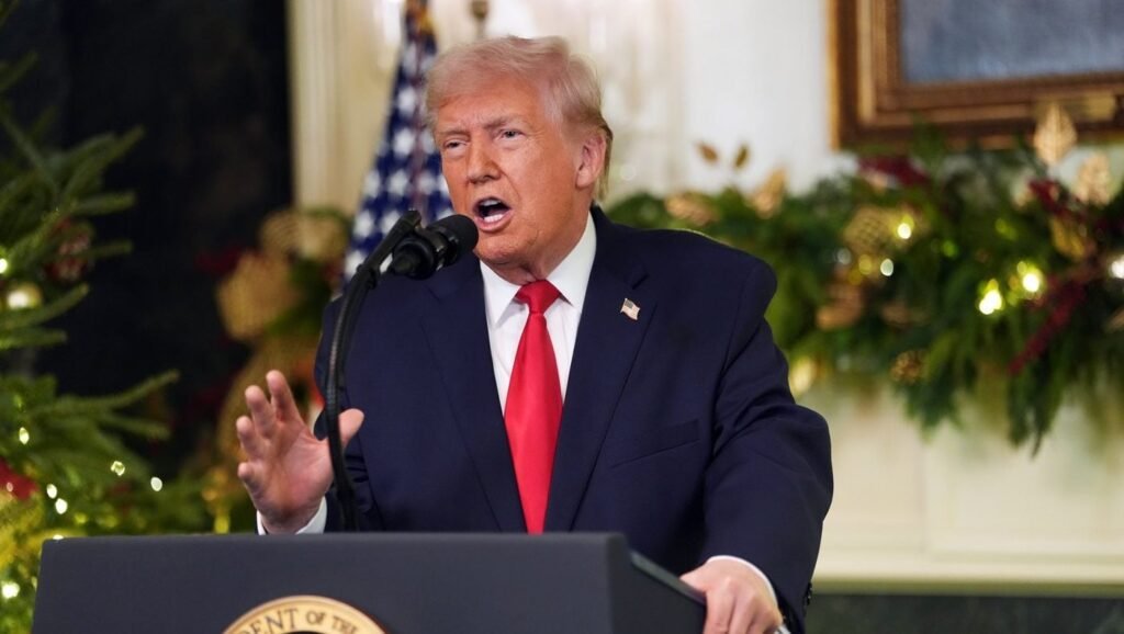 Președintele Donald Trump se adresează națiunii de la Casa Albă. Trump vorbeste de la tribuna, poarta un costum albastru închis, camasa alba si cravată roșie și gesticulează cu mâna